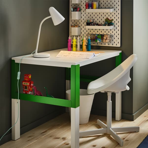 A white/green desk, a white work lamp, a white pegboard with accessories, paint in bottles and a white children’s desk chair.