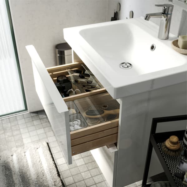 A white/grey bathroom where a wash stand drawer is open and smoked boxes inside help organising bathroom necessities.