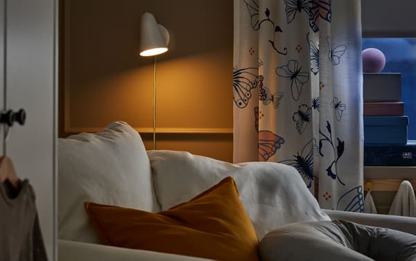 A white GRÖNLID chaise longue in the corner of a darkened room, lit by an IKEA FUBBLA white LED wall lamp.