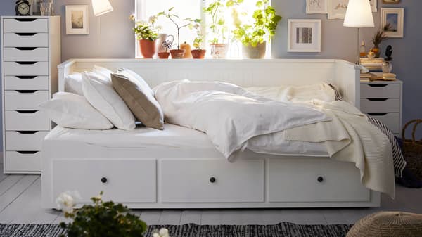 A white HEMNES daybed in the middle of a room pulled out as a bed with a white comforter and pillows on it