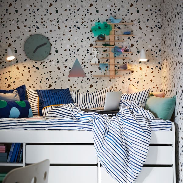 A white IKEA SLÄKT bed, with blue and white striped bed linen, with two IKEA FUBBBLA white LED wall lamps in a bedroom.
