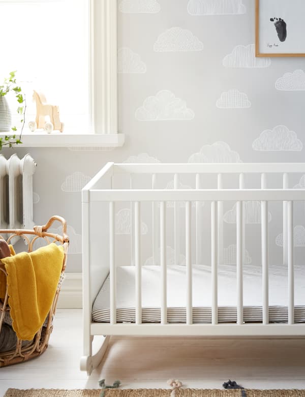 A white IKEA SOLGUL rocking cot on white wooden floorboards with SOLGUL yellow blanket and a natural textile rug.