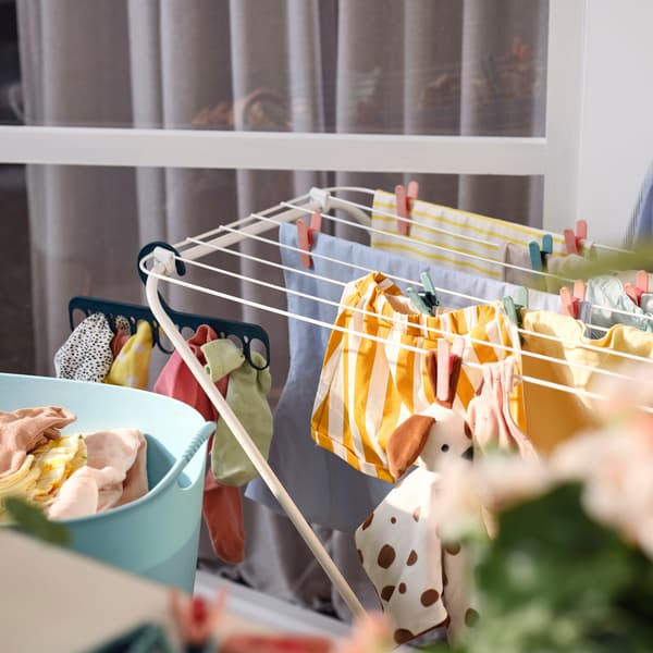 A white JÄLL drying rack with clothes held by clothes pegs and a hanger with 8 grip clips, plus a flexible laundry basket.