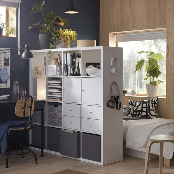 A white KALLAX shelf acting as a room seperator filled with storage.