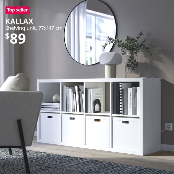 A white KALLAX shelving unit in a living room setting placed against the wall next to the window and sofa seating. A red "Top seller" label is on the top left of image, with white text below that reads: KALLAX, Shelving unit, 77x147 cm. Price: $89.