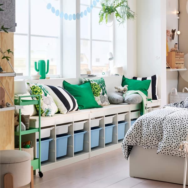 A white kids storage unit with green and black/white pillows on top.