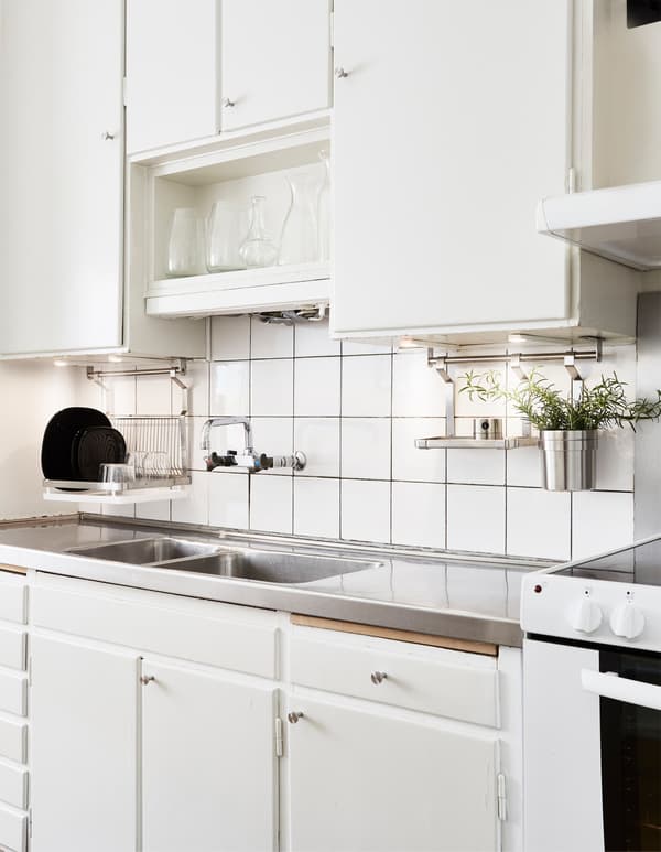 A white kitchen area with a deep stainless steel sink, lit with under-cabinet lighting.