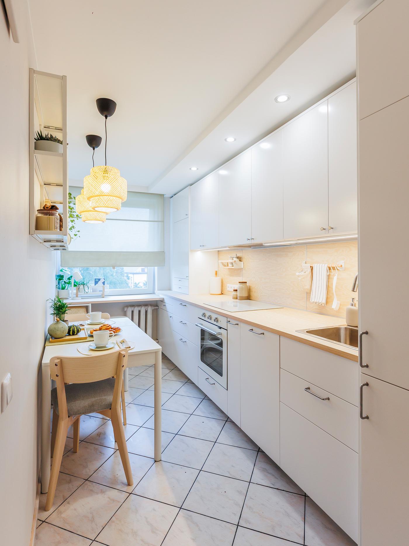 A white kitchen arranged in a single line, featuring a dining table and chairs on the opposite side, and two handmade pendant lamps hanging above the table.