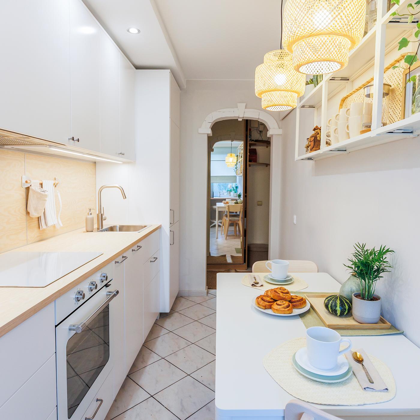 A white kitchen with a table set for breakfast, open shelving displaying plates, and two pendant lamps hanging above the table.