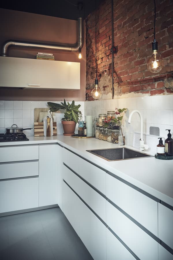 A white kitchen with an exposed brick wall.