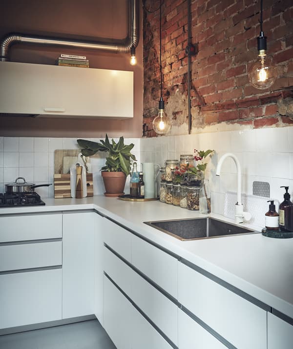 A white kitchen with an exposed brick wall.
