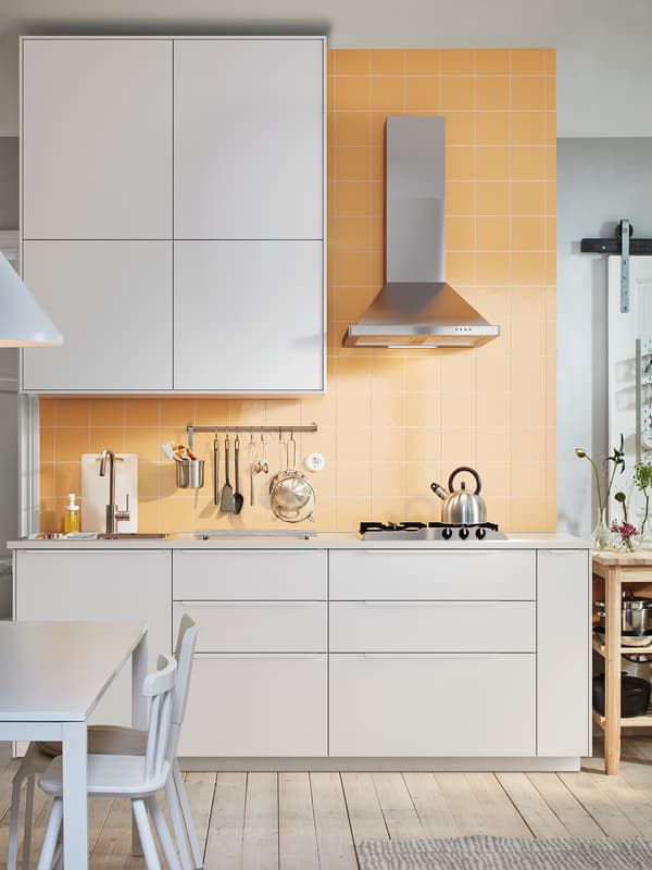 A white kitchen with white cabinets, a wall mounted extractor hood in stainless steel and a white table and chairs.