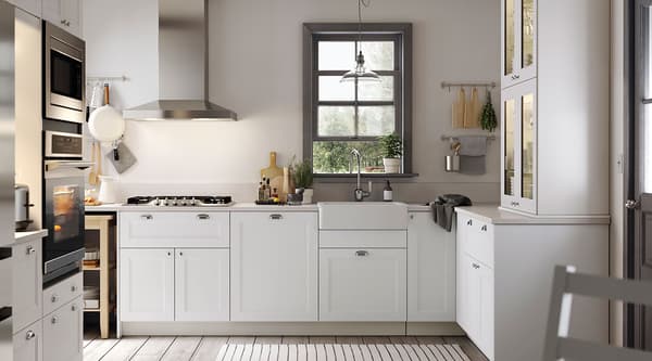 A white kitchen with white drawers and cabinets with glass doors and a stainless steel sink with a visible front.