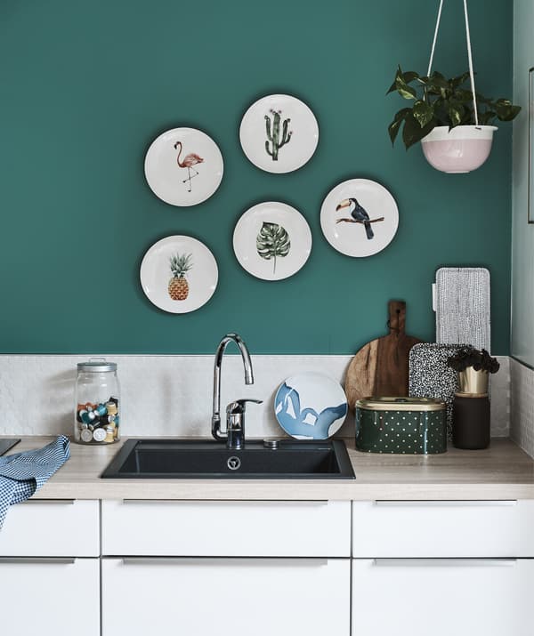 A white kitchen with wooden worktops and a green wall with decorative plates.
