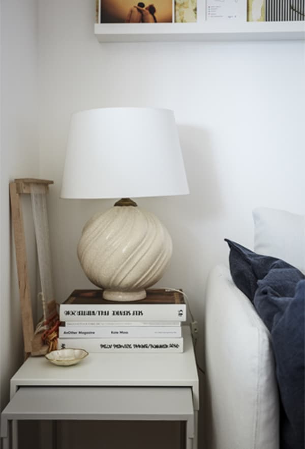 A white lamp on a pile of books on a nest of side tables.
