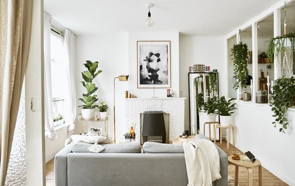 A white living room with sofa, fireplace, plants and stools used as side tables.