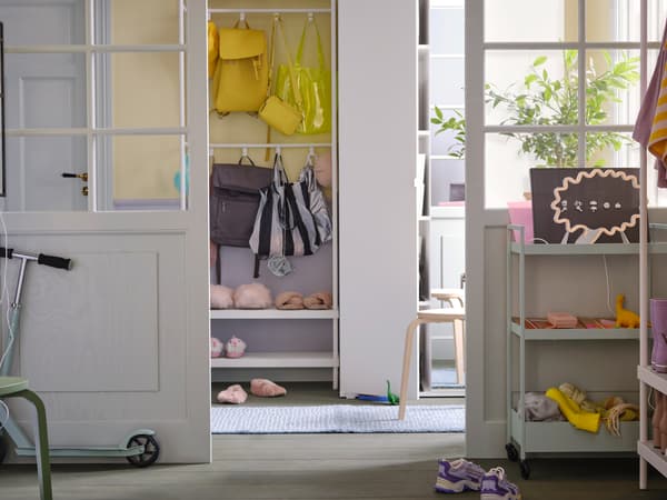 A white MACKAPÄR coat rack with shoe storage unit holding shoes and bags stands beside a white VIHALS wardrobe in a hallway.