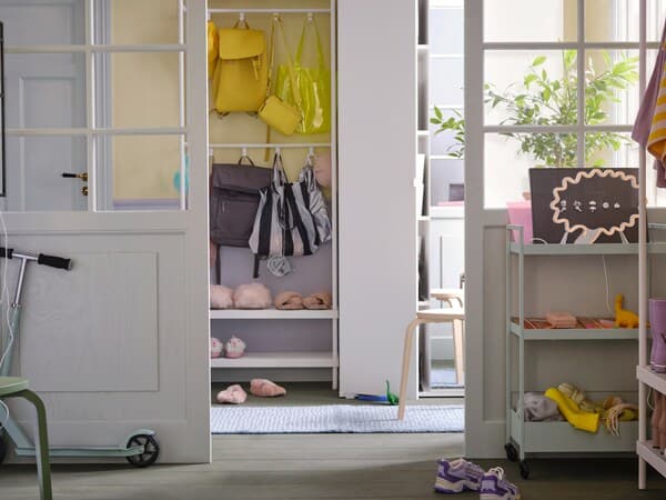 A white MACKAPÄR coat rack with shoe storage unit holding shoes and bags stands beside a white VIHAL