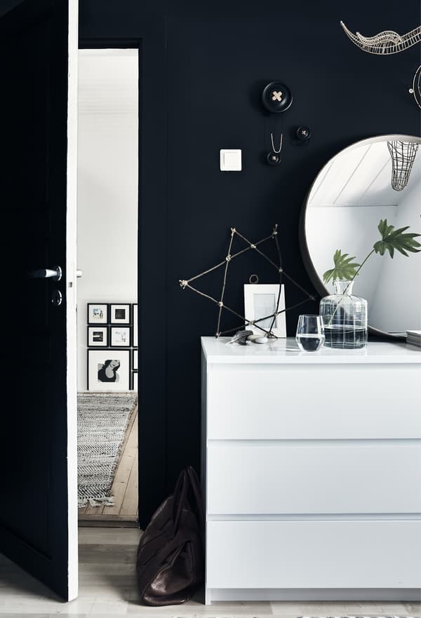 A white MALM chest of drawers with a round mirror above, against a black wall.