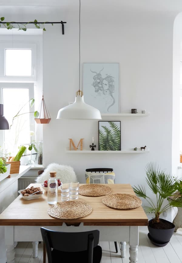 A white metal pendant lamp hangs over a square wooden dining table.