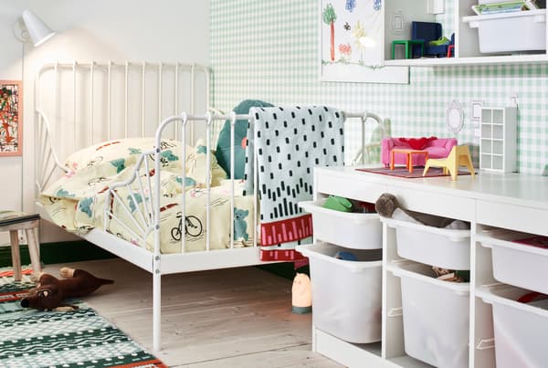 A white MINNEN extendable bed in the corner of a children’s room, lined with toys, reading light and storage.