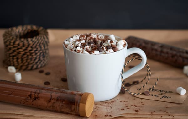 A white mug of hot cocoa is topped with chocolate chips and mini marshmallows.