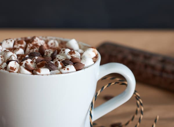 A white mug of hot cocoa is topped with chocolate chips and mini marshmallows.