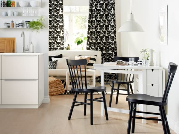 A white NORDEN table with two drop-leaves together with black chairs in a small monochrome living space.