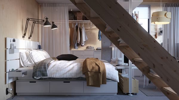 A white NORDLI bed with storage and headboard covered in VITKLÖVER bed linen, in front of an ELVARLI storage combination.
