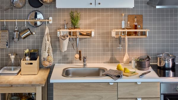 A white/oak effect ENHET kitchen by a gray-tiled wall with a birch rail, two birch wall shelves and a white wall cabinet.