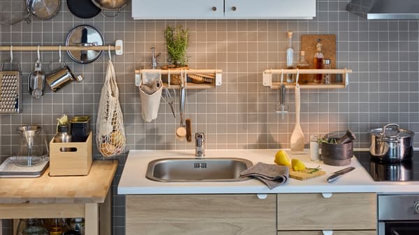 A white/oak effect ENHET kitchen by a grey-tiled wall with a birch rail, two birch wall shelves and a white wall cabinet.