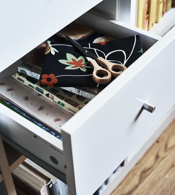A white open drawer in a KALLAX unit, with sewing material inside.