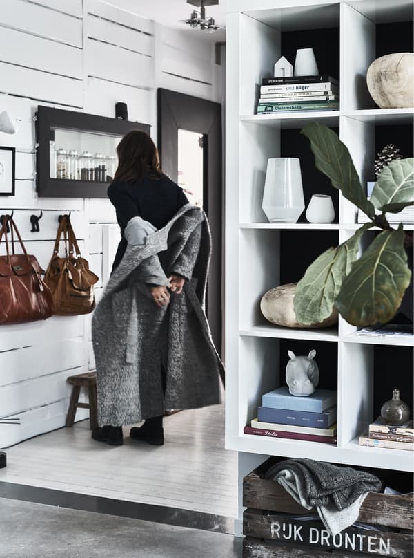 A white open storage unit filled with keepsakes and books and in the back a hallway with white shiplap walls.
