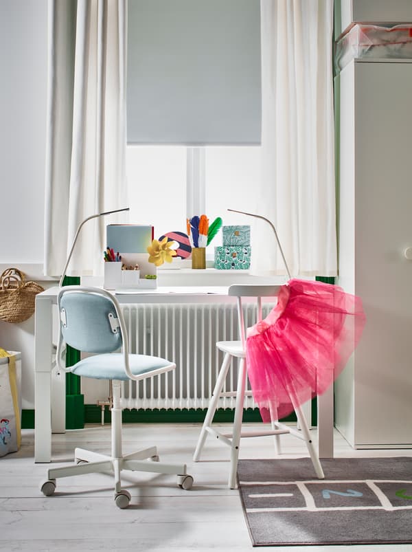 A white PÅHL desk and AGAM junior chair placed next to a sunlit window in a light, wood-floor children’s room.