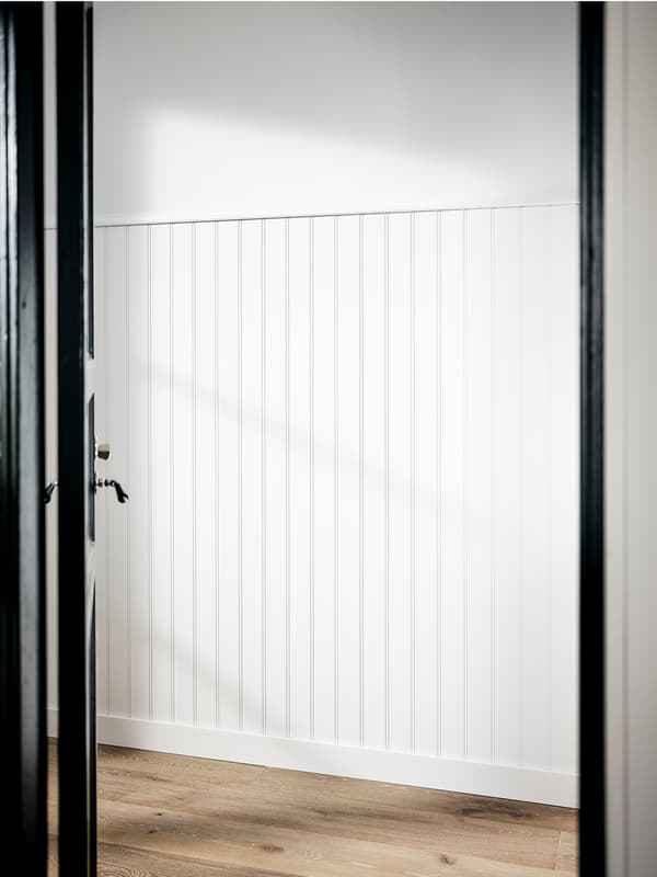 A white-painted hallway with wood paneling halfway up the wall and a wooden floor.