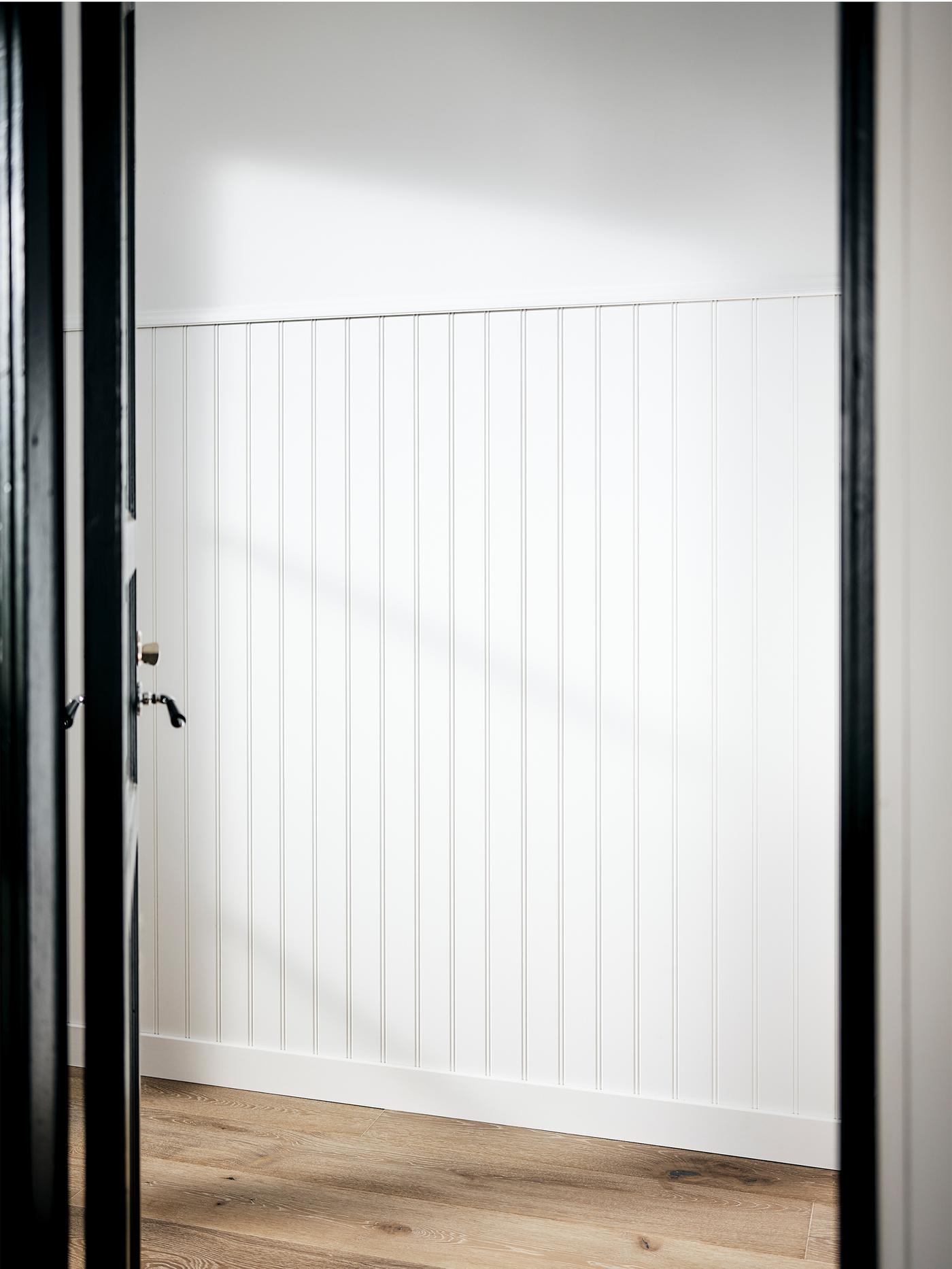 A white-painted hallway with wood panelling halfway up the wall and a wooden floor.