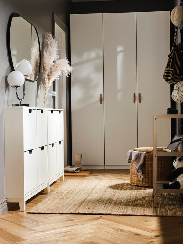 A white PAX/FORSAND wardrobe at the end of a hallway, with two white STÄLL shoe cabinets on one side with a mirror above it.