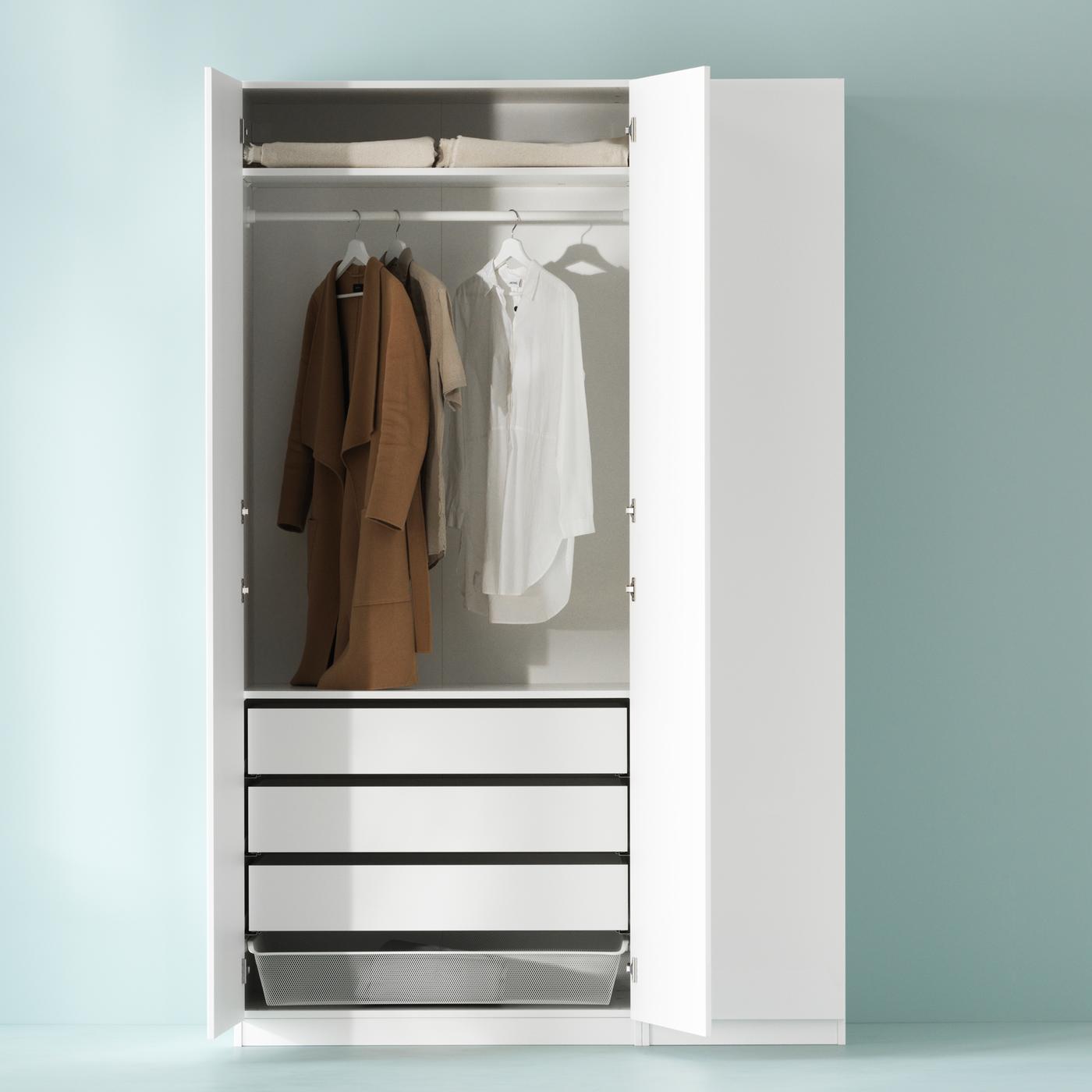 A white PAX wardrobe combination against a pale green wall with two doors open and three pieces of clothing on hangers.