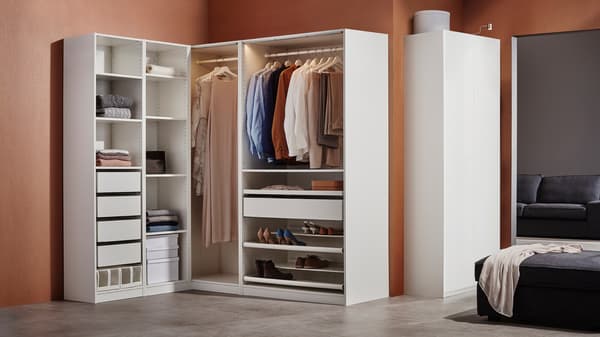 A white PAX wardrobe corner combination against a brown wall contains drawers, boxes, shoe racks, and hanging clothes.