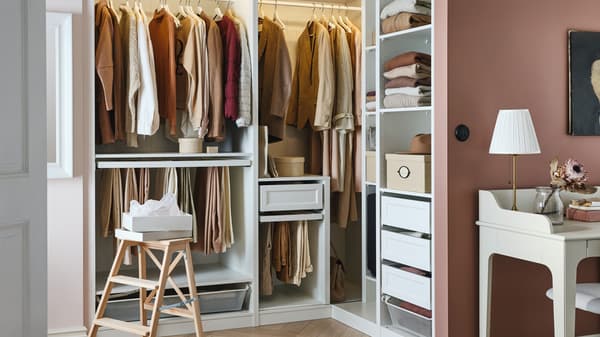 A white PAX wardrobe corner combination against a brown wall contains drawers, boxes, shoe racks and hanging clothes.