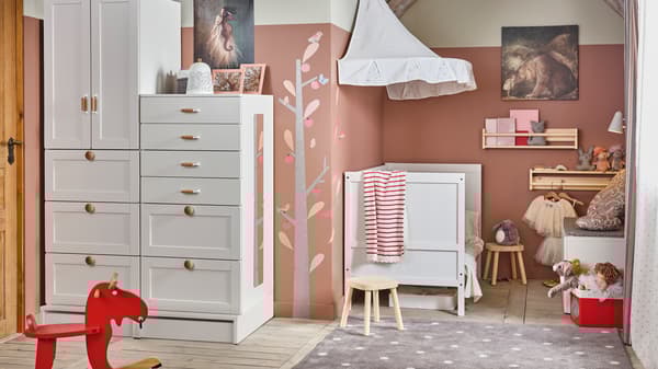 A white/pink traditional children’s room with SMÅSTAD storage, a SUNDVIK crib, and FLISAT children’s stools.