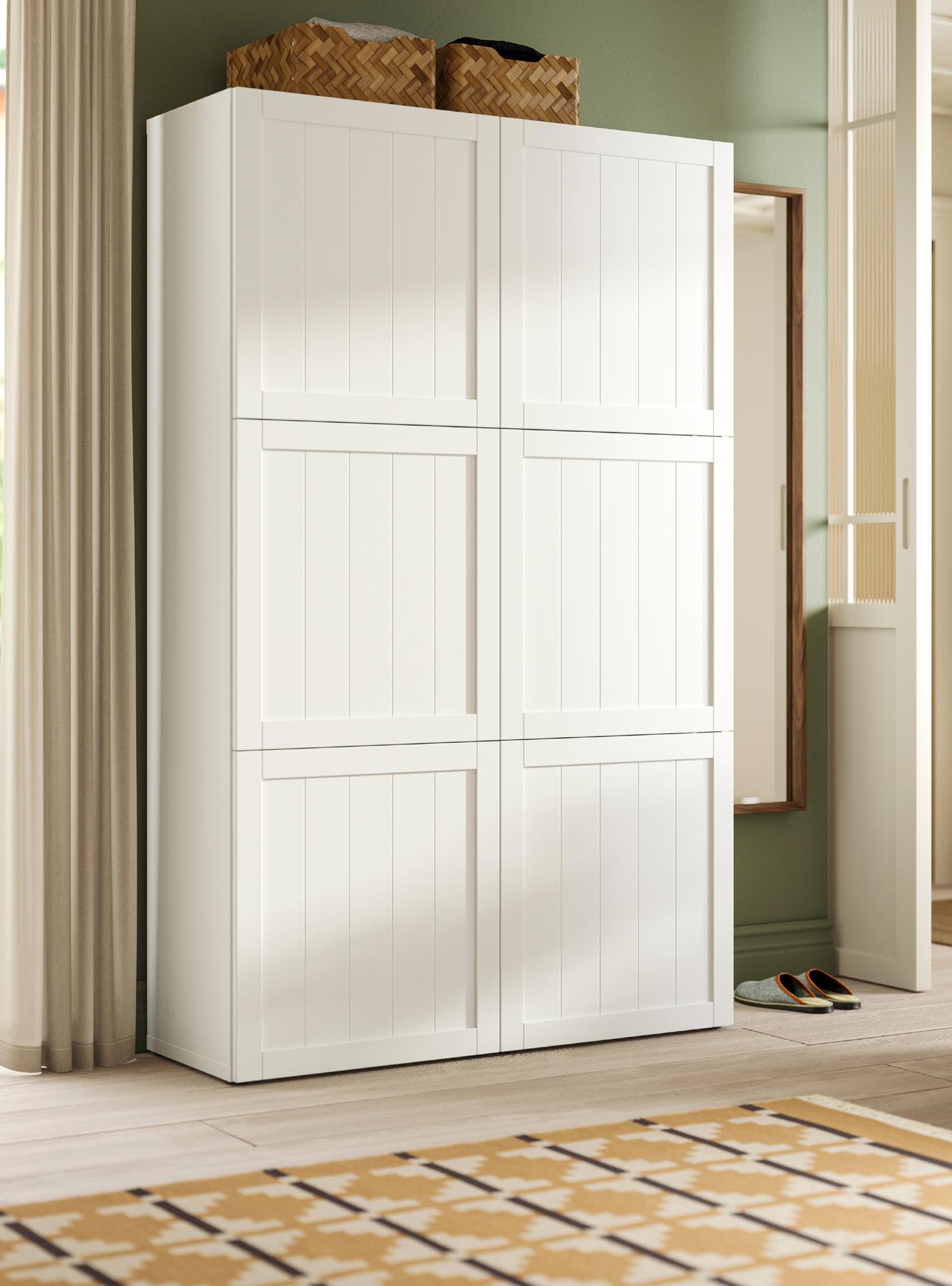 A white/PIPMAKARE white BESTÅ storage combination with 6 doors in a bright room with two baskets on top and a mirror by it.