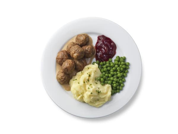A white plate with mashed potatoes, peas, and meatballs with gravy.