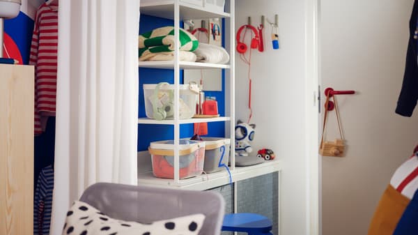 A white PLATSA open wardrobe with sliding dark grey LARKOLLEN doors near a door, holding storage boxes and folded clothes.