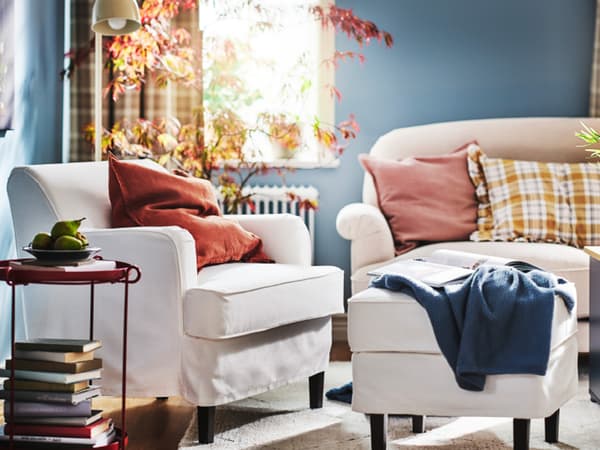 A white ROCKSJÖN armchair and a white ROCKSJÖN footstool stand beside a light beige ESSEBODA sofa in a bright living room.