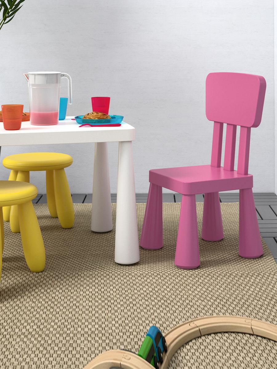 A white room featuring a children table, chair and stools with toy dinnerware on top.