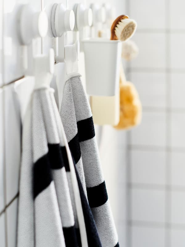 A white shelf mounted high up on the wall in a hallway with hooks on the bottom shelf to hang coats, backpacks and coats.