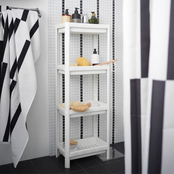 A white shelf unit is standing in a black/white shower and is storing shower necessities like shampoos and more.