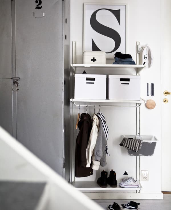A white shelving unit in a hallway with boxes, and a low-level hanging rail and wire basket.