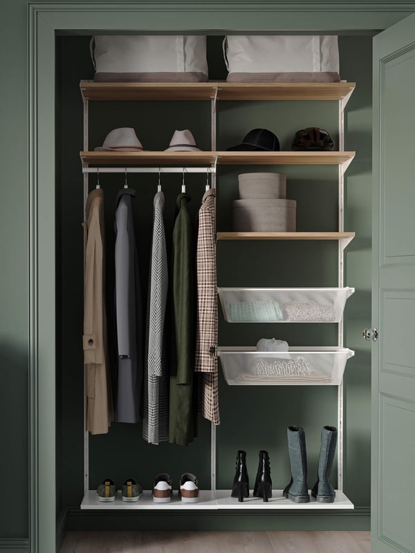 A white shelving unit with wooden shelves mounted in a closet with green walls.